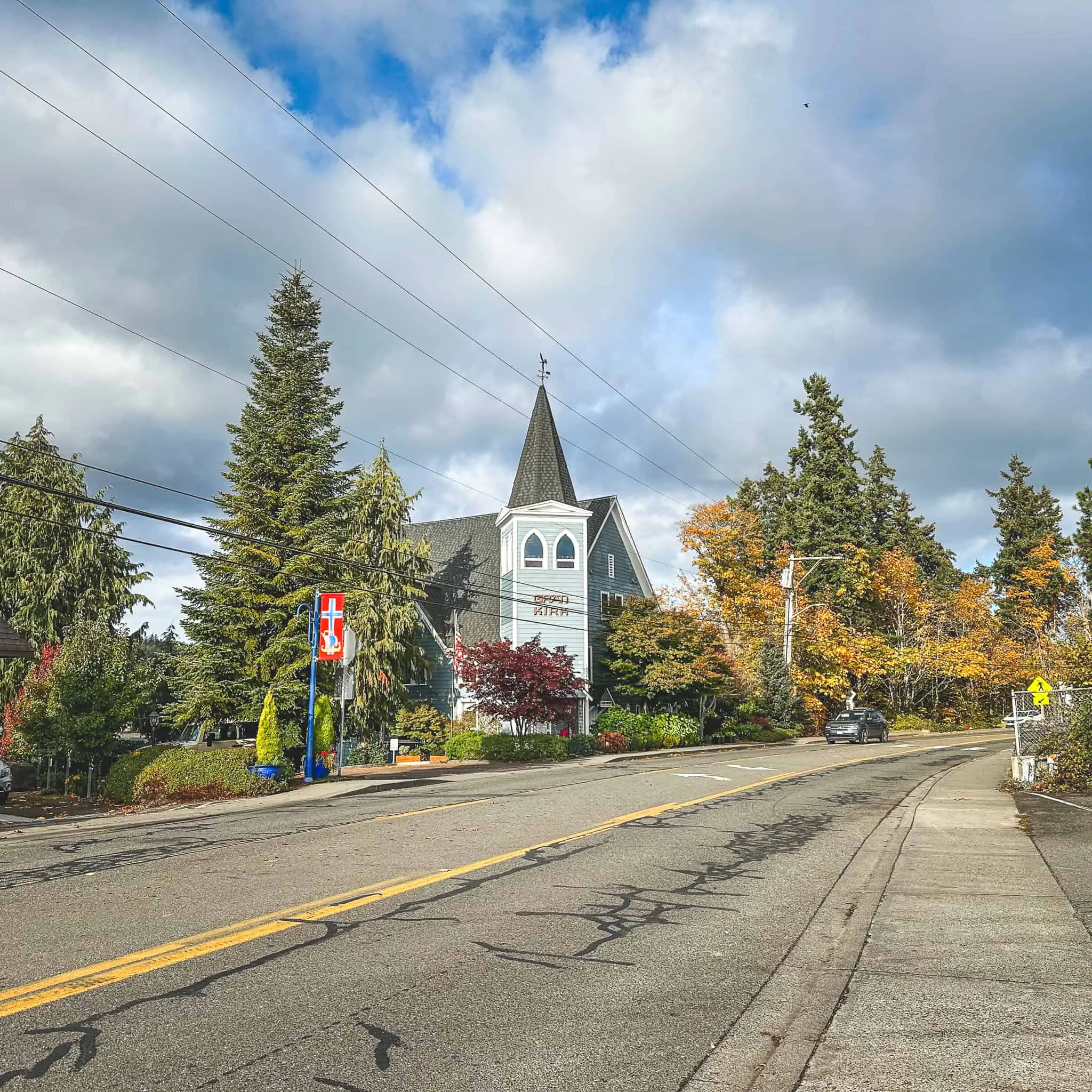 Scenic view of a church with a tall steeple in Poulsbo, surrounded by colorful trees and a cloudysky.